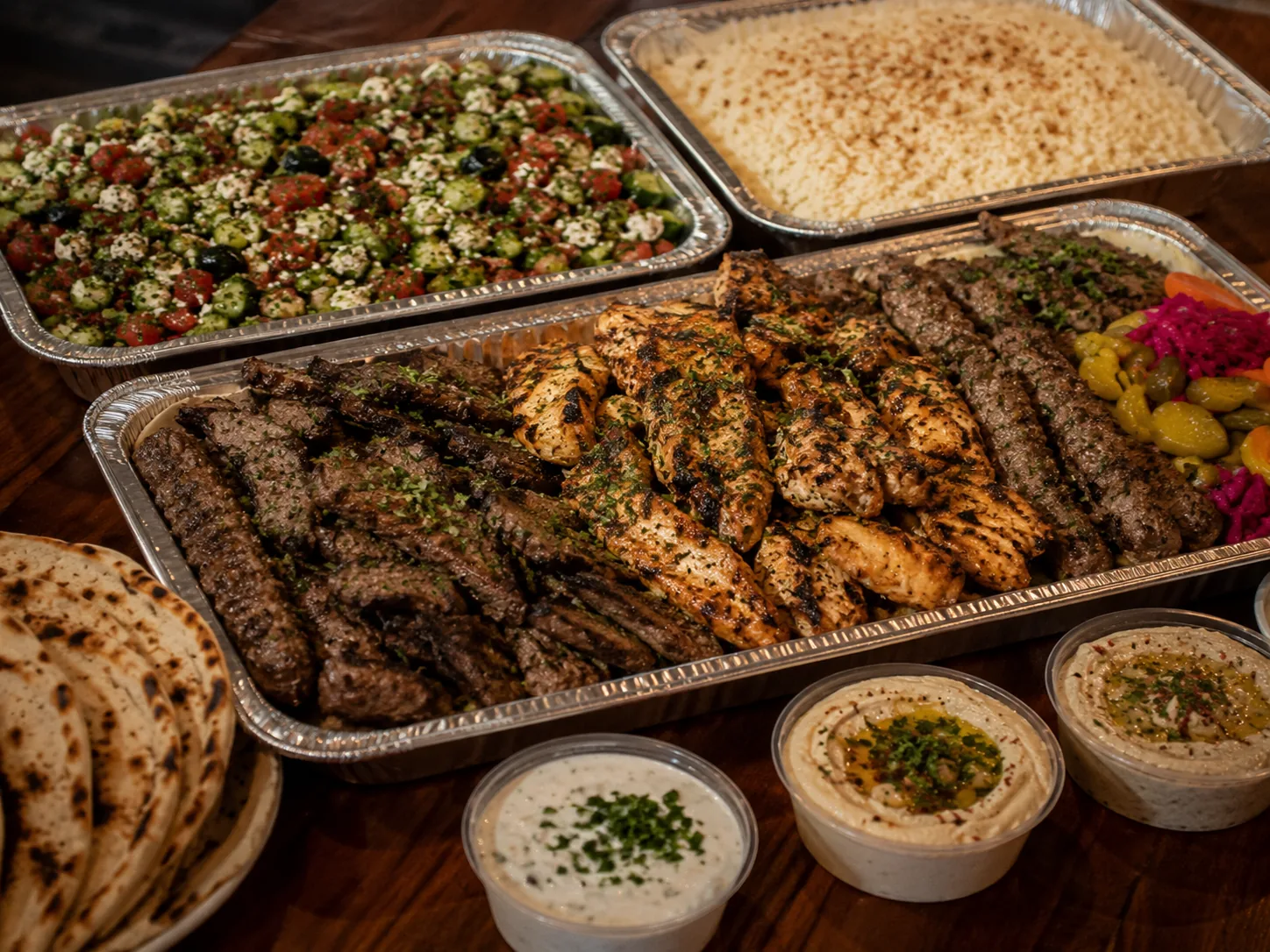 Family-style Mediterranean tray with grilled meats, rice, pita, salads, and sauces