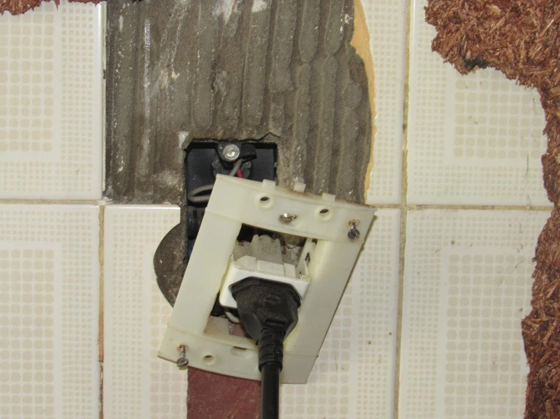 A damaged wall outlet with a loose plugged-in cord.